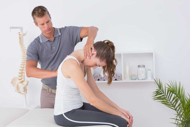 A chiropractor gently checking posture and mobility on a smiling school-aged child in a clinic setting.